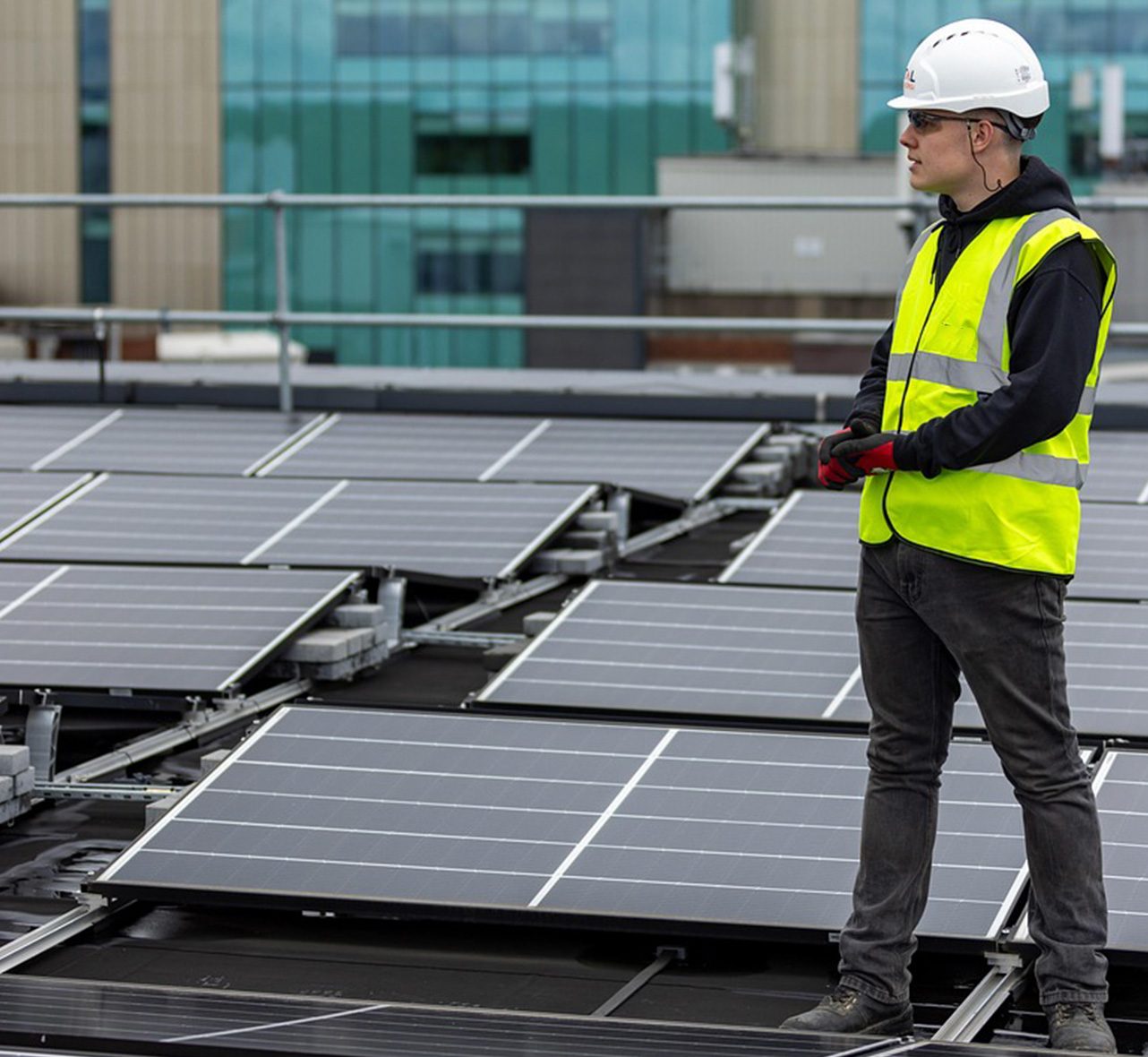 Un homme en équipement de sécurité, à genoux sur un toit, est en train d'installer un panneau solaire.